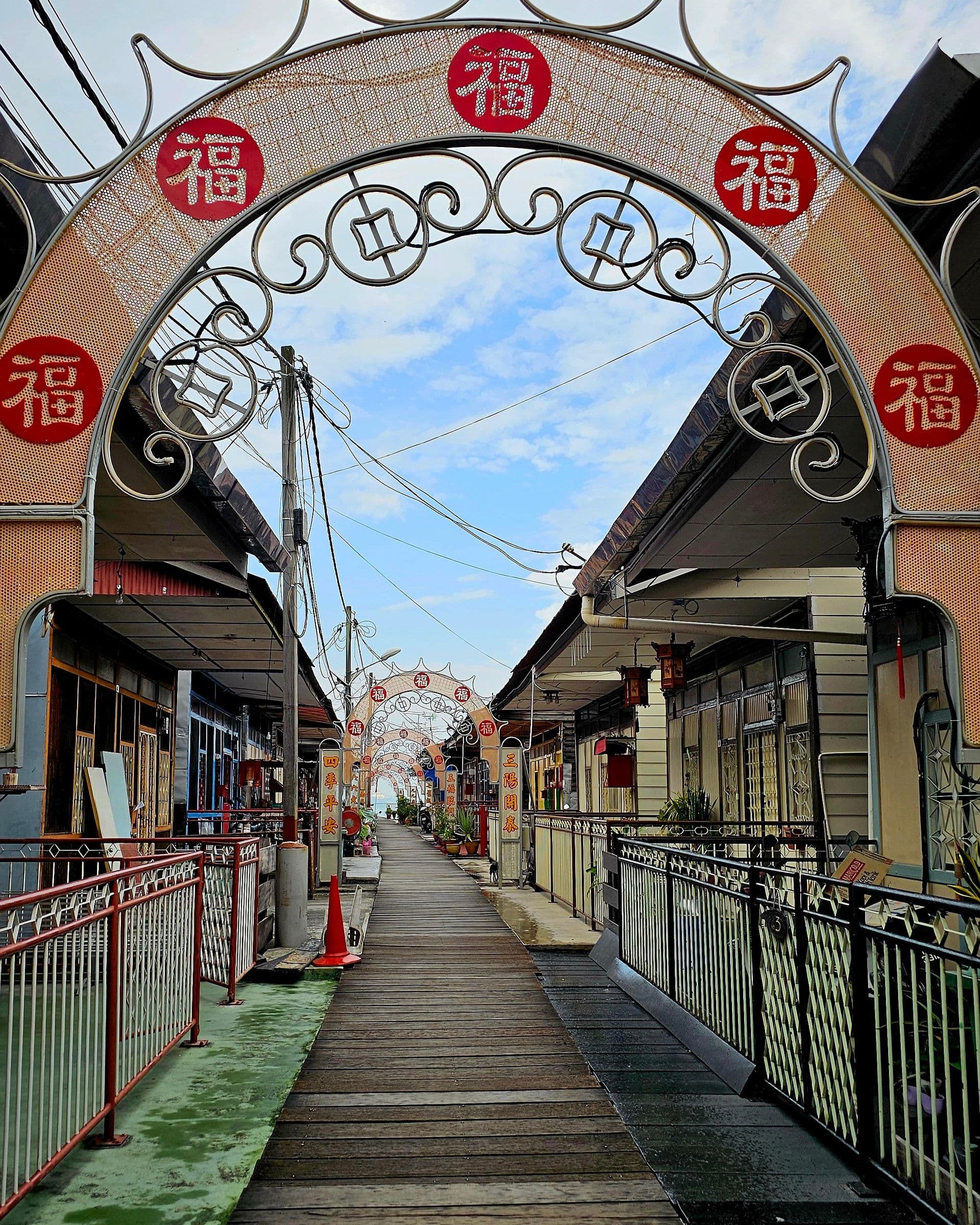 Ornamental arches over the wooden boardwalk of a clan jetty, stilt houses on either side